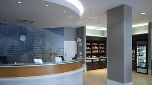 A reception area with a curved counter, a clock, and a wall with text. There is a 'The Market' section with shelves and a refrigerator in the background. - SpringHill Suites by Marriott San Antonio Alamo Plaza/Convention Center (San Antonio)