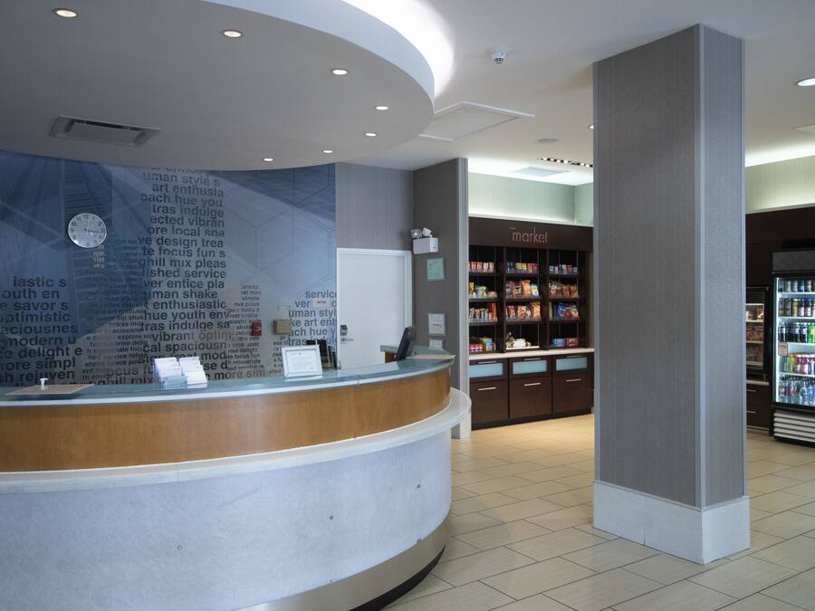 A reception area with a curved counter, a clock, and a wall with text. There is a 'The Market' section with shelves and a refrigerator in the background.