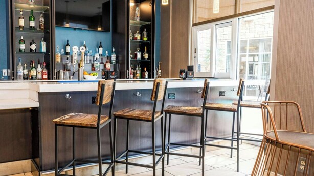 A bar area with multiple stools and shelves stocked with bottles. - SpringHill Suites by Marriott San Antonio Alamo Plaza/Convention Center (San Antonio)
