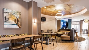 A modern hotel lobby with a long wooden bench, multiple seating options, a TV mounted on the wall, and a curved ceiling design. - SpringHill Suites by Marriott San Antonio Alamo Plaza/Convention Center (San Antonio)