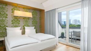A hotel room with a bed, a desk, a window with a view of the city, and a balcony with outdoor furniture. - NH Frankfurt Messe (Frankfurt)
