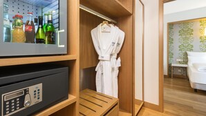 A hotel room with a minibar, a robe hanging on a rack, and a bed with a white pillow.