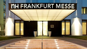 The entrance of NH Frankfurt Messe hotel with a modern facade, large glass windows, and a prominent entrance with steps leading up to the doors. - NH Frankfurt Messe (Frankfurt)
