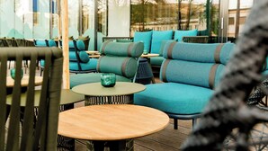 An outdoor seating area with teal upholstered sofas and round wooden tables. - Motel One Salzburg-Süd (Salzburg)