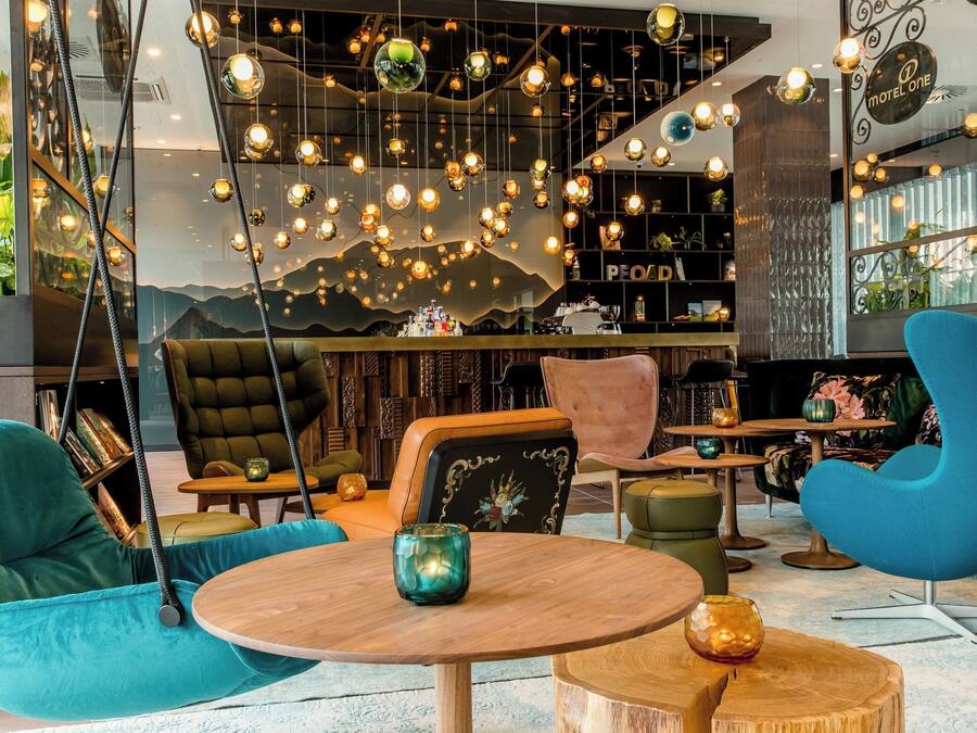 Un área de descanso moderna con luces esféricas colgantes, asientos cómodos y una estantería.