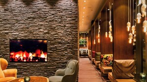 A modern lounge area with a stone wall, comfortable seating, a flat-screen TV, and pendant lighting. - Motel One Salzburg-Süd (Salzburg)