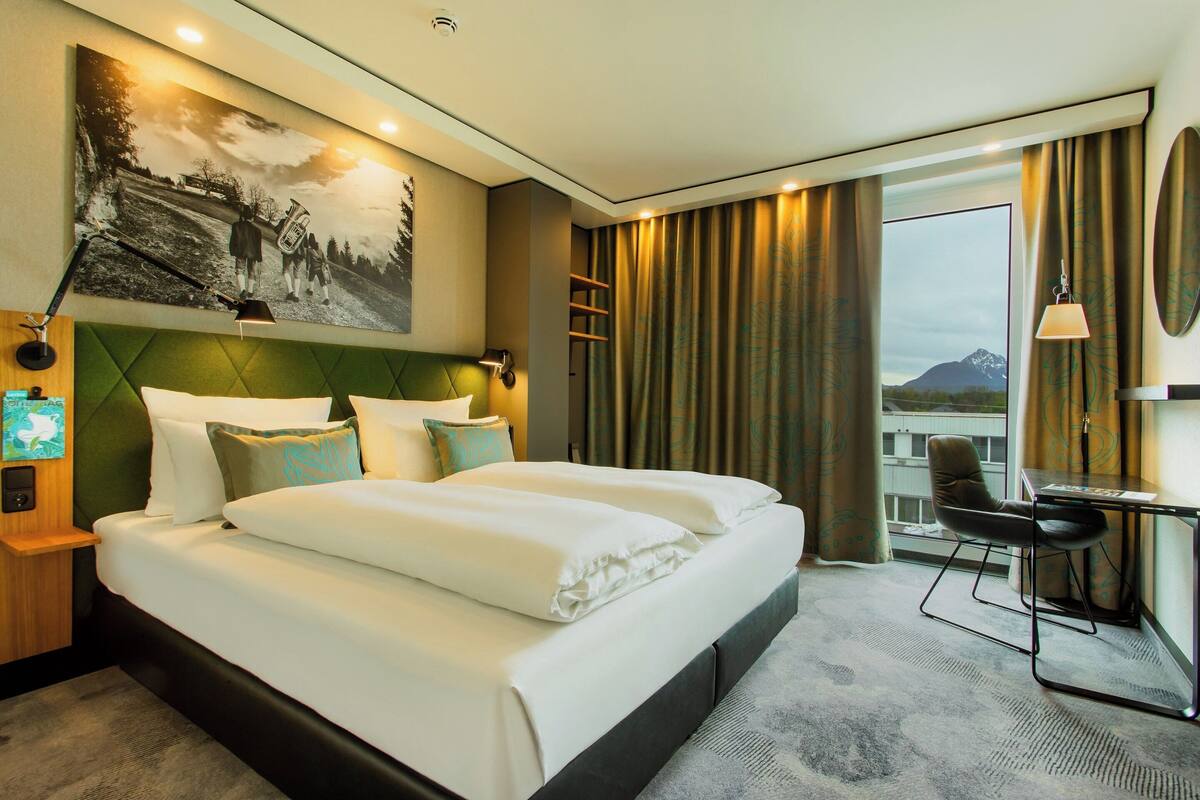 A hotel room with a large bed, a desk, and a view of mountains through the window.