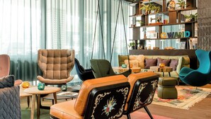 A modern living room with a sofa, armchairs, a coffee table, and a bookshelf. - Motel One Salzburg-Süd (Salzburg)
