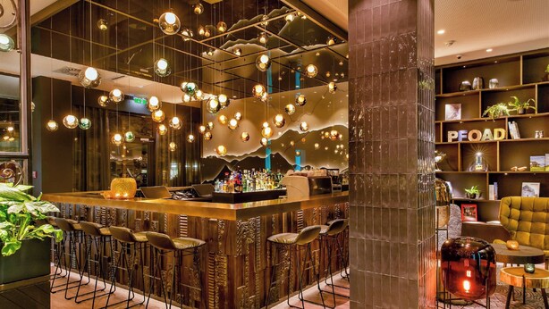 A bar area with multiple stools, a bar counter, and hanging spherical light fixtures. - Motel One Salzburg-Süd (Salzburg)