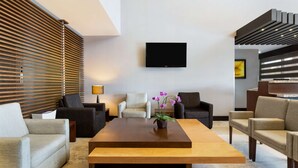 A modern living room with a large wooden coffee table, several sofas, and a flat-screen TV mounted on the wall. - DoubleTree by Hilton Hotel Queretaro (Querétaro)