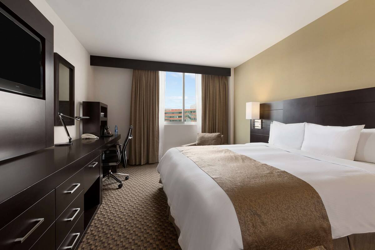 Habitación de hotel con una cama grande, un escritorio con televisión de pantalla plana, una silla y vistas a la ciudad desde la ventana.