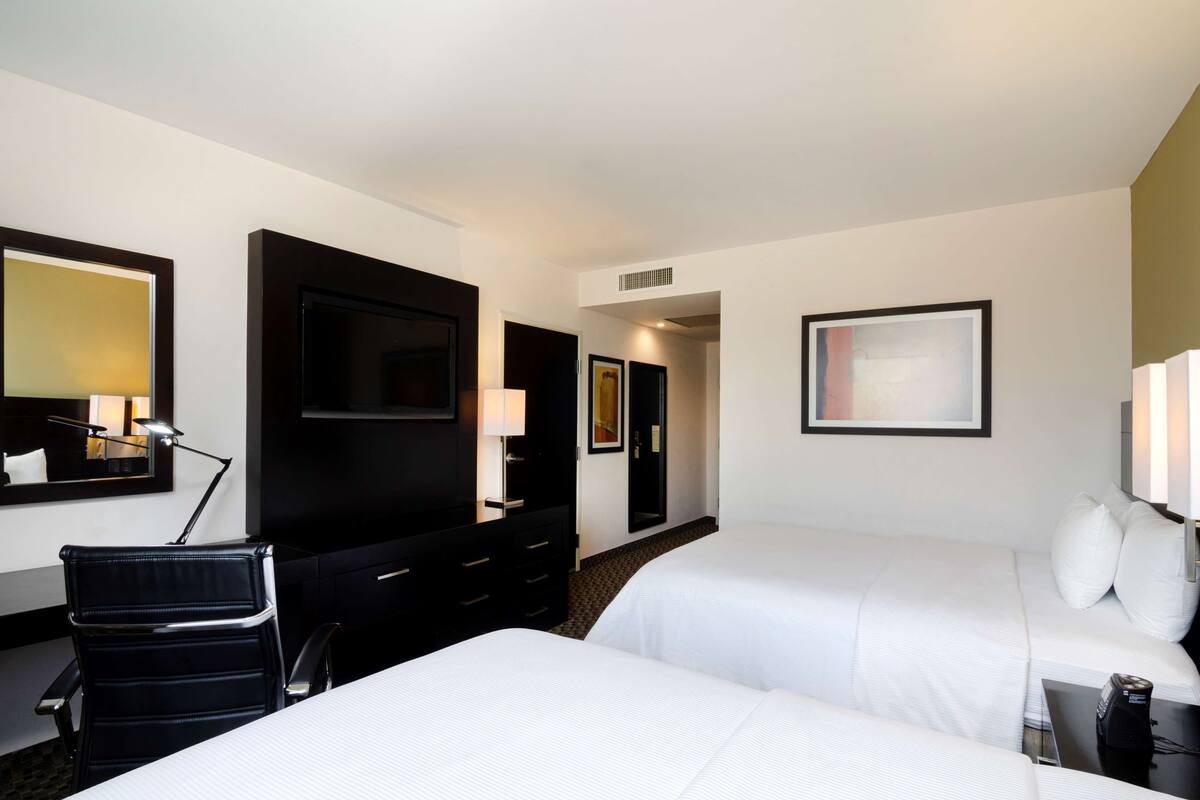 Habitación de hotel con dos camas, un escritorio con silla, televisor y espejo.