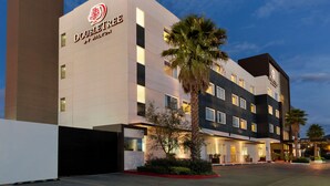 A modern hotel with a prominent DoubleTree logo, featuring a clean facade, multiple windows, and a parking area with palm trees. - DoubleTree by Hilton Hotel Queretaro (Querétaro)