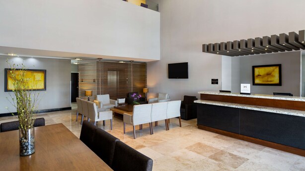 A modern hotel lobby with a reception desk, seating area, and a dining table. - DoubleTree by Hilton Hotel Queretaro (Querétaro)