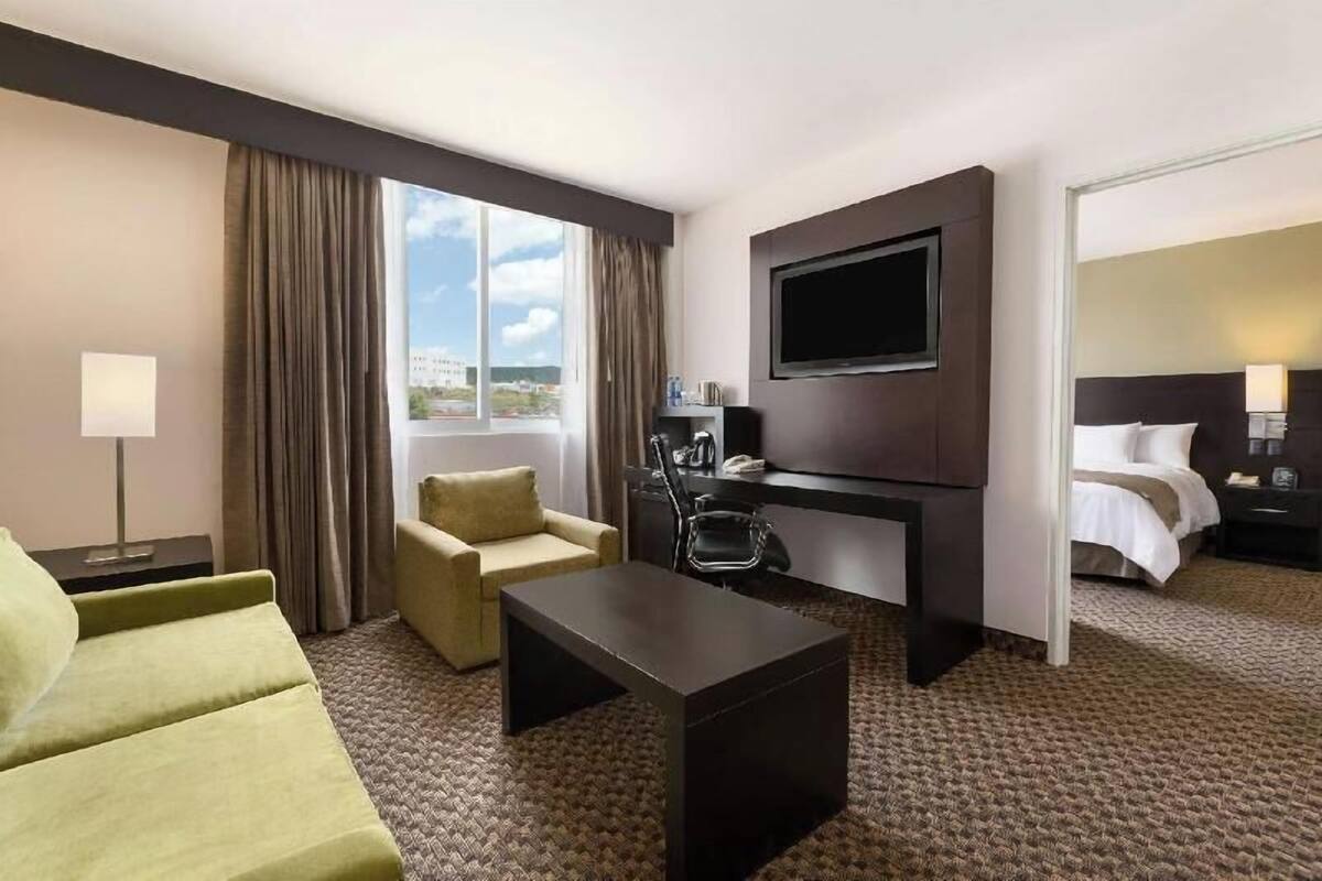 Una habitación de hotel con cama, escritorio, televisor, sofá y ventana.