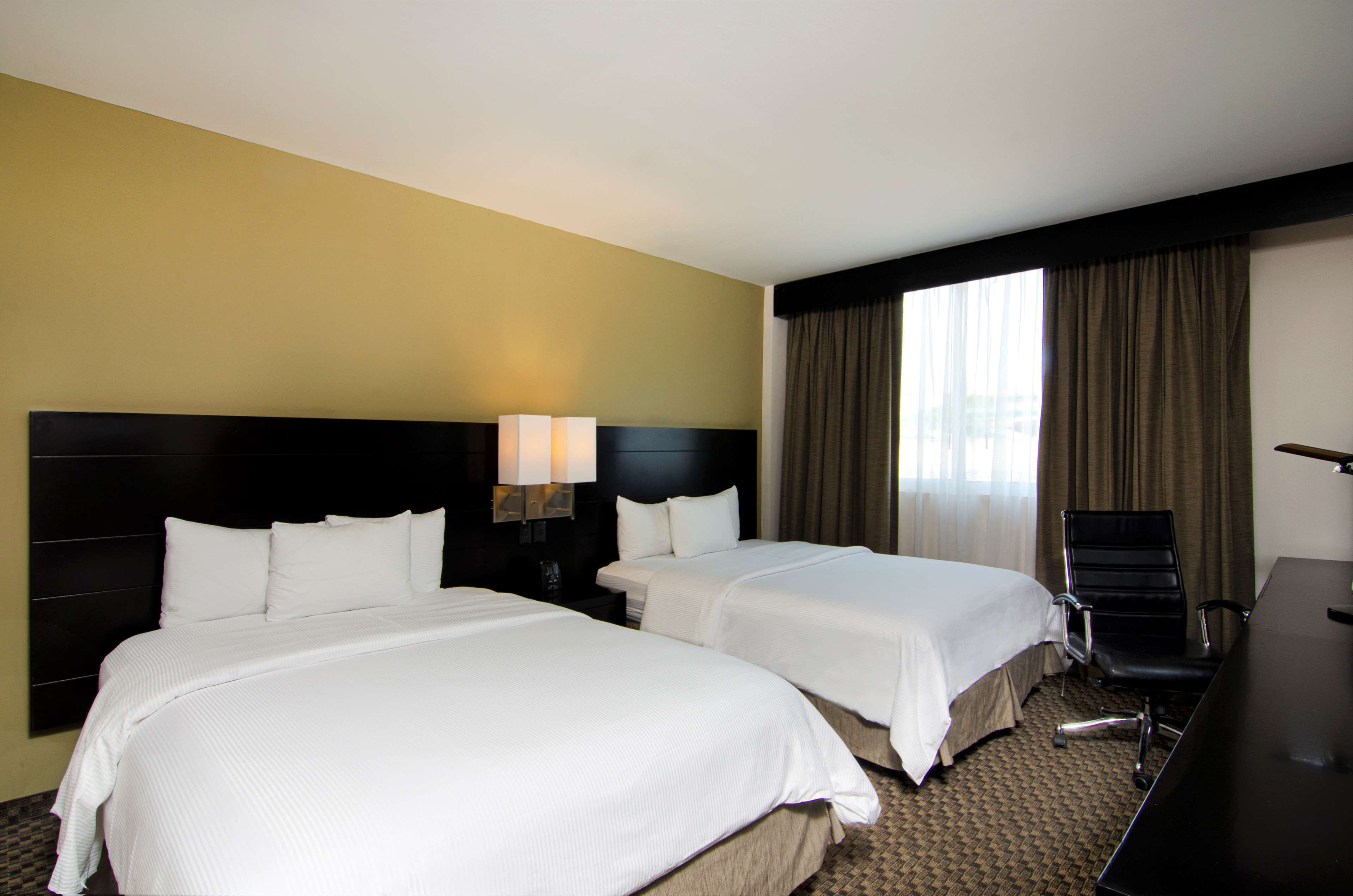 A hotel room with two beds, a desk, and a chair.