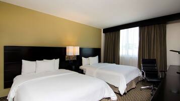 A hotel room with two beds, a desk, and a chair.
