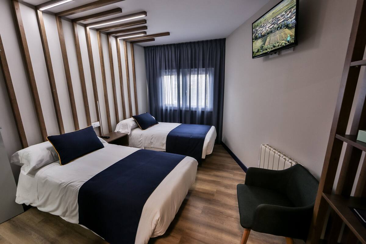 Ein Hotelzimmer mit zwei Betten, einem Sessel, einem Heizkörper und einem Fernseher an der Wand.