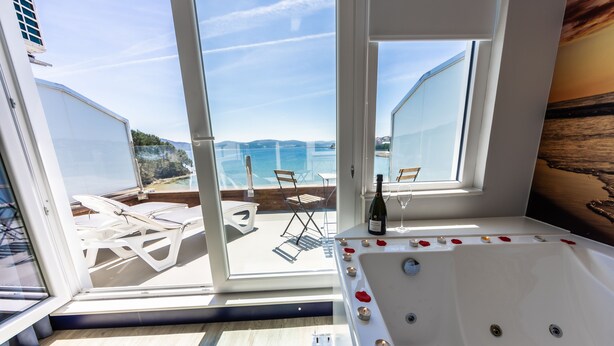 Un balcón con vista al mar, un jacuzzi con velas y una botella de vino.