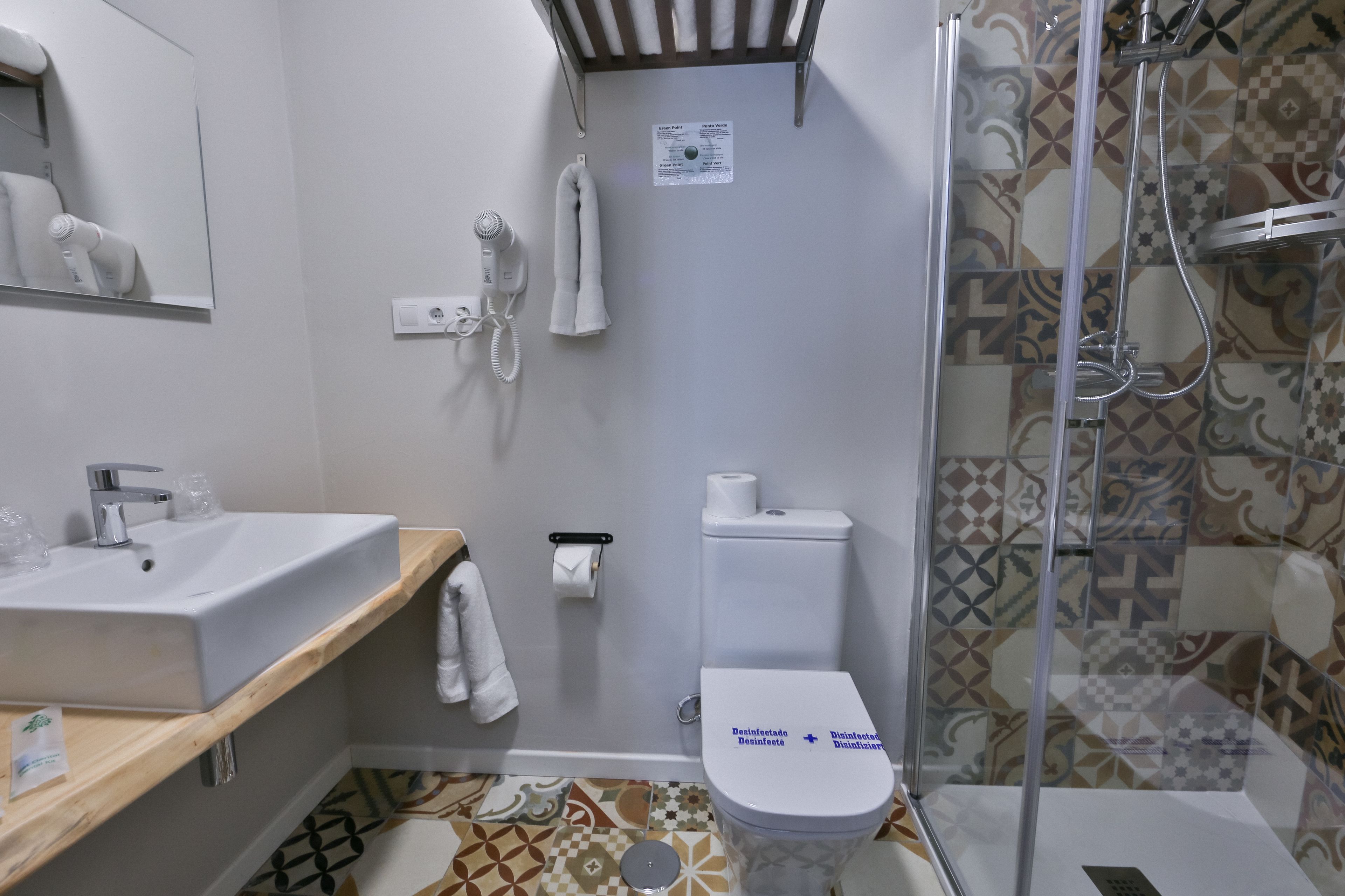 Ein Badezimmer mit Waschbecken, Toilette und Dusche. Ein Handtuch hängt an der Wand und ein Papierhandtuchspender ist vorhanden.