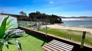 Un balcón con césped artificial, sillas de madera y vista al mar.