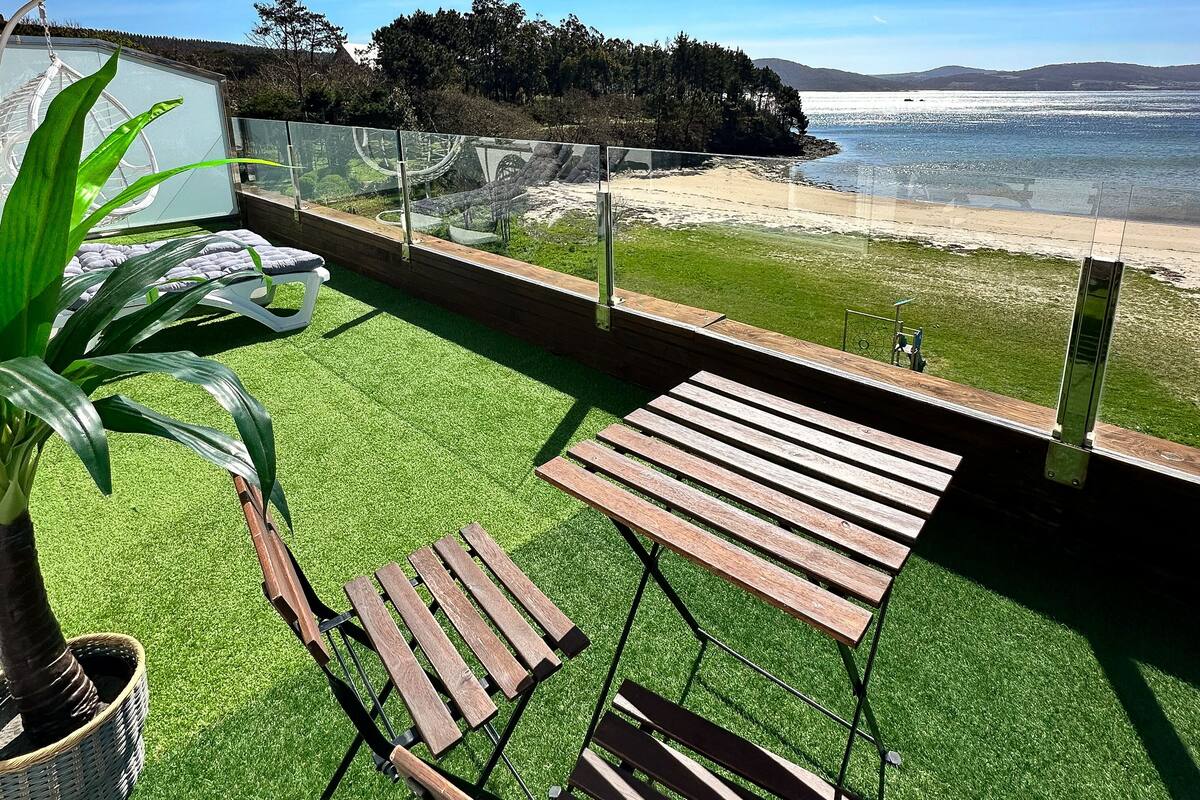 Ein Balkon mit künstlichem Rasen, Holzstühlen und Blick auf das Meer.
