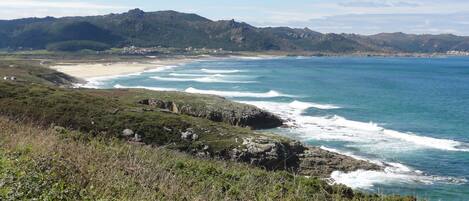 Un paisaje costero con una playa, costa rocosa y montañas al fondo.