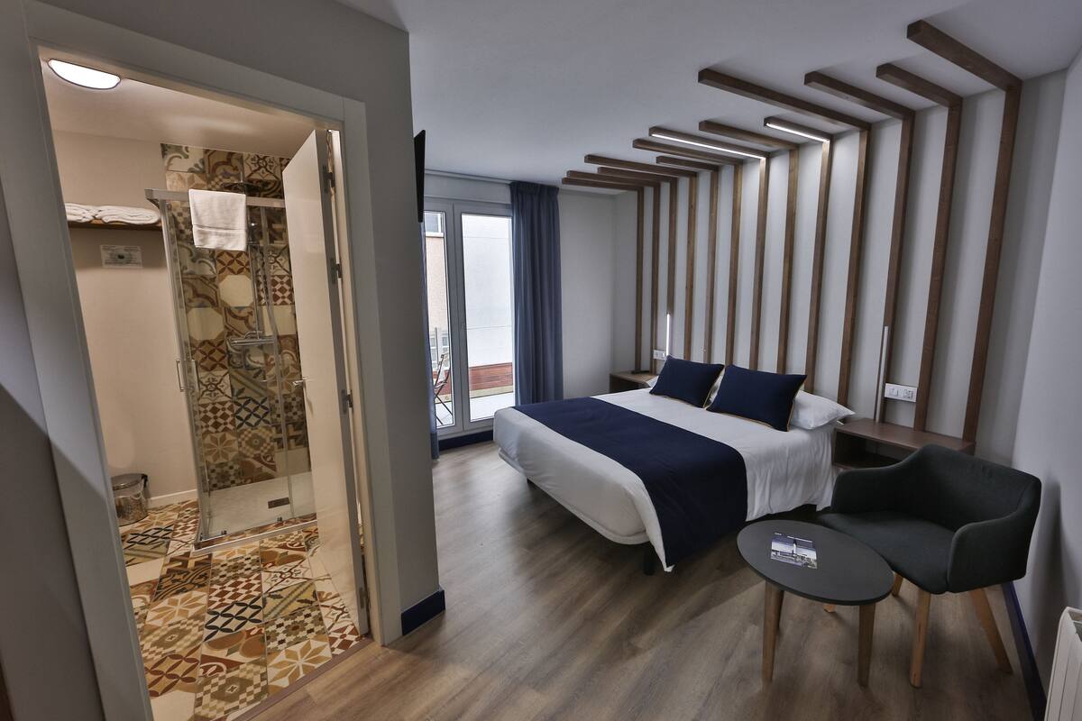 Ein modernes Hotelzimmer mit einem großen Bett, einem kleinen Tisch, einem Stuhl und einer Duschkabine.