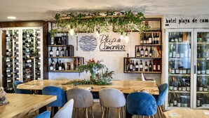 Interior de restaurante con barra de madera, sillas azules y estanterías para vino.
