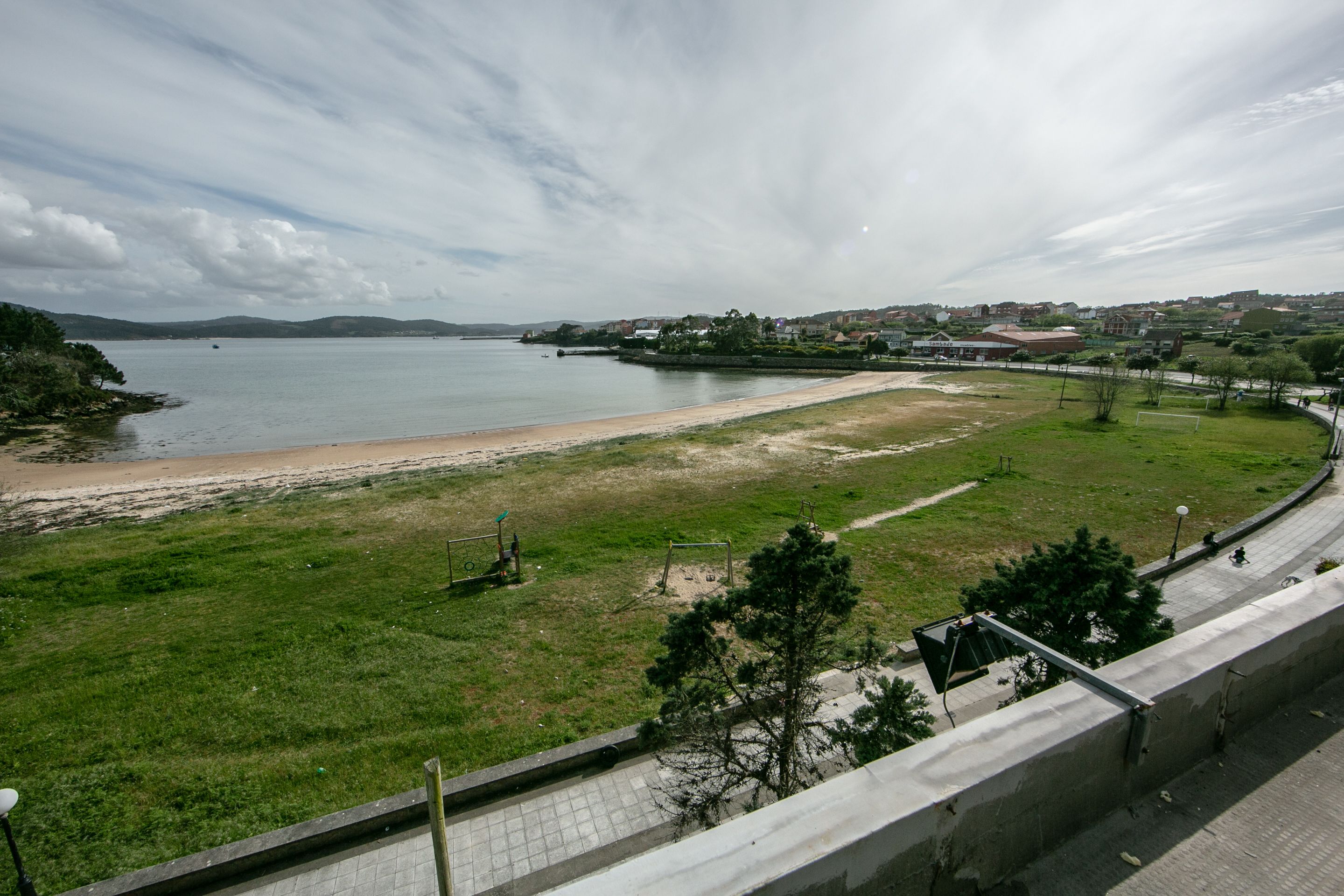A coastal view with a beach, grassy areas, and a paved walkway.