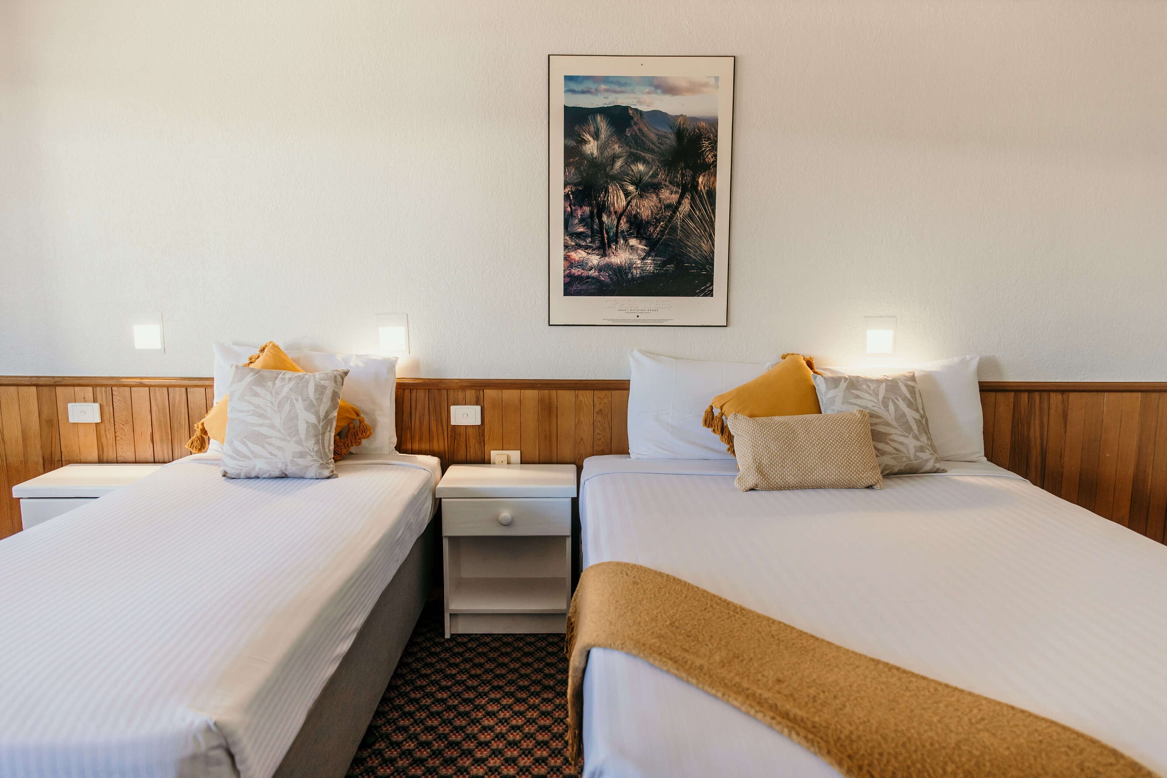 A hotel room with two beds, a nightstand, a framed picture on the wall, and a patterned carpet.