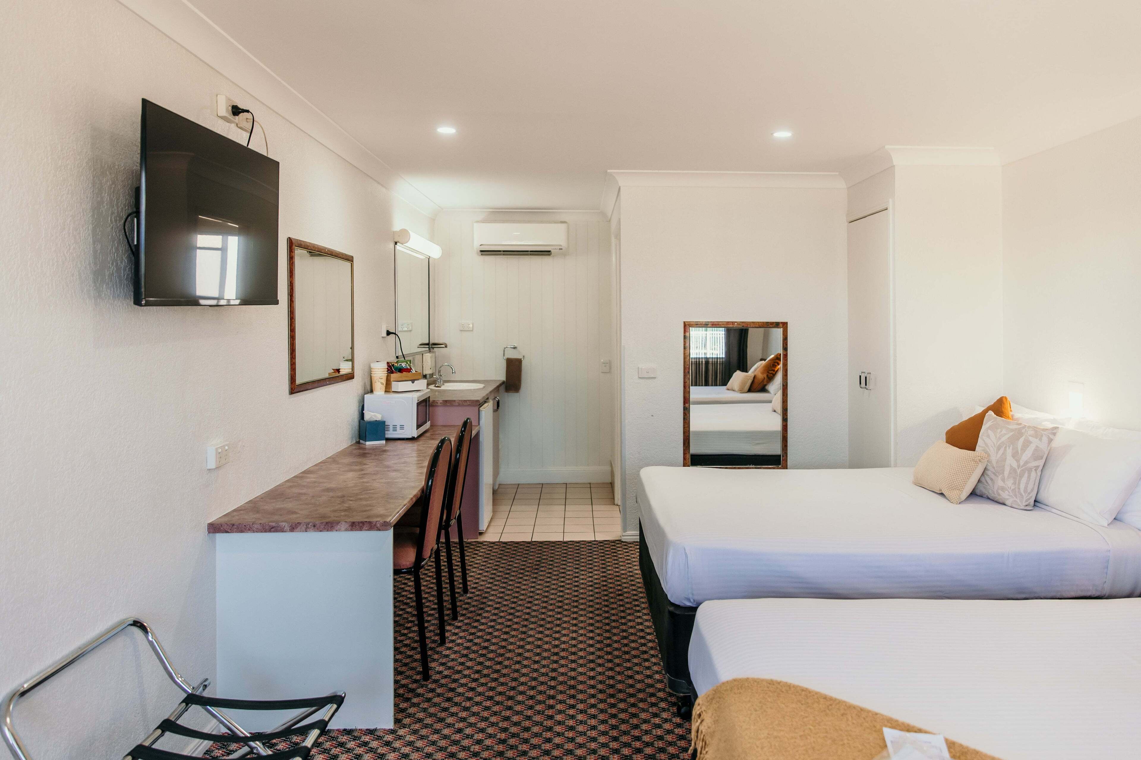Una habitación de hotel con cama, escritorio, silla, televisor y espejo.