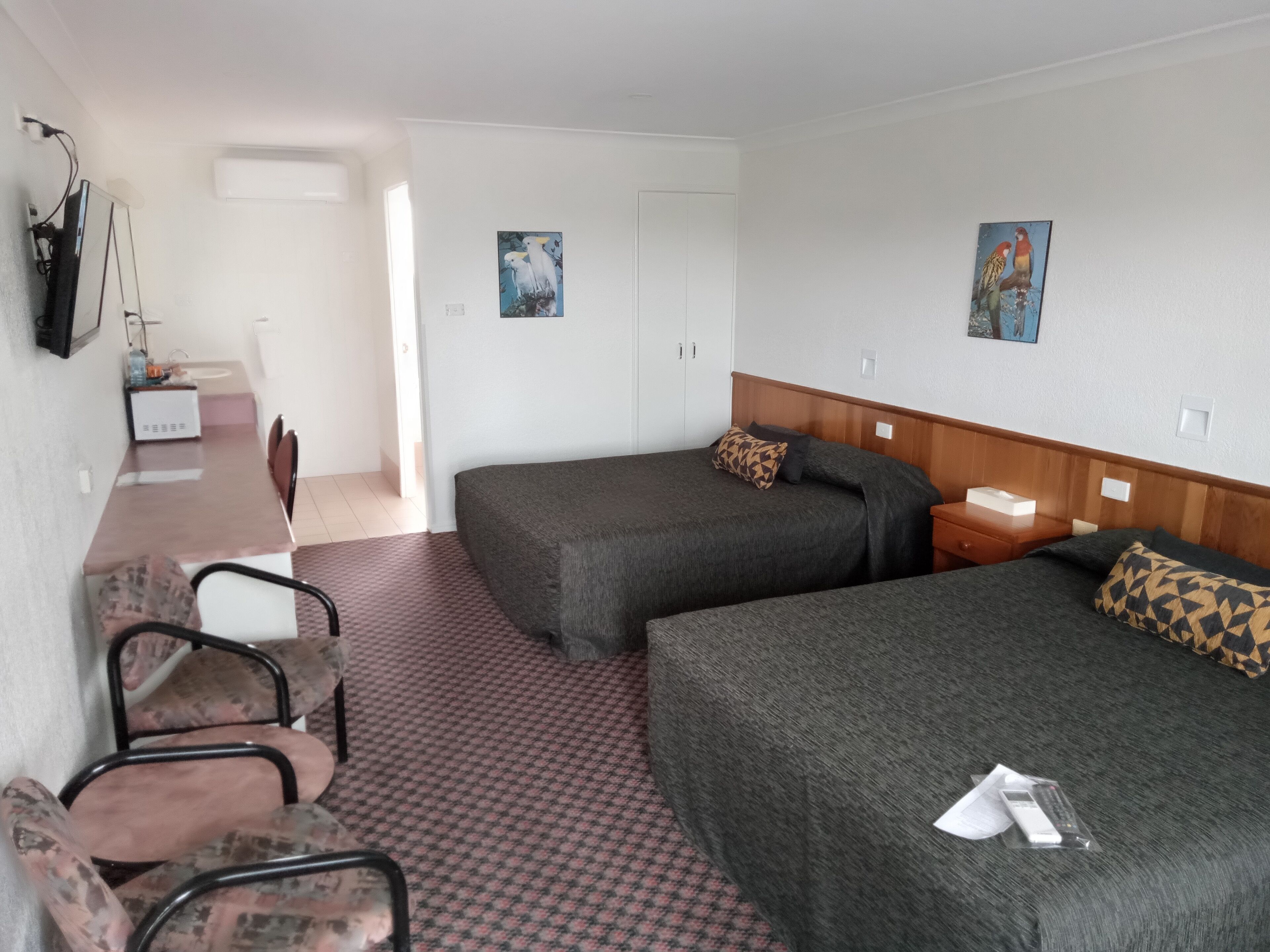 A hotel room with two single beds, a desk with a chair, a TV, and artwork on the walls.