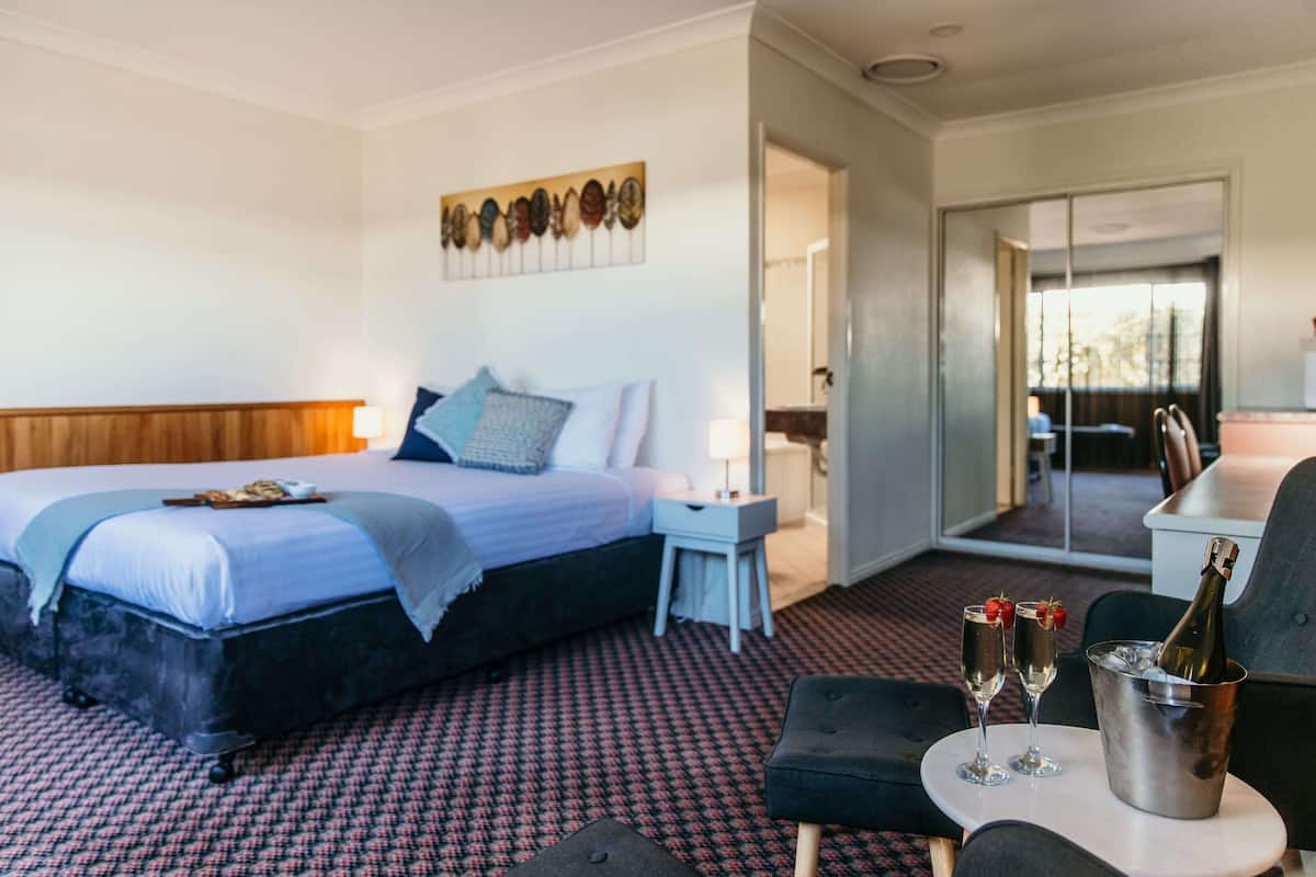 A hotel room with a bed, a small table with drinks, and a balcony.