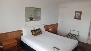 A hotel room with a bed, a bedside table, a nightstand, a mirror, a wardrobe, and a small shelf.