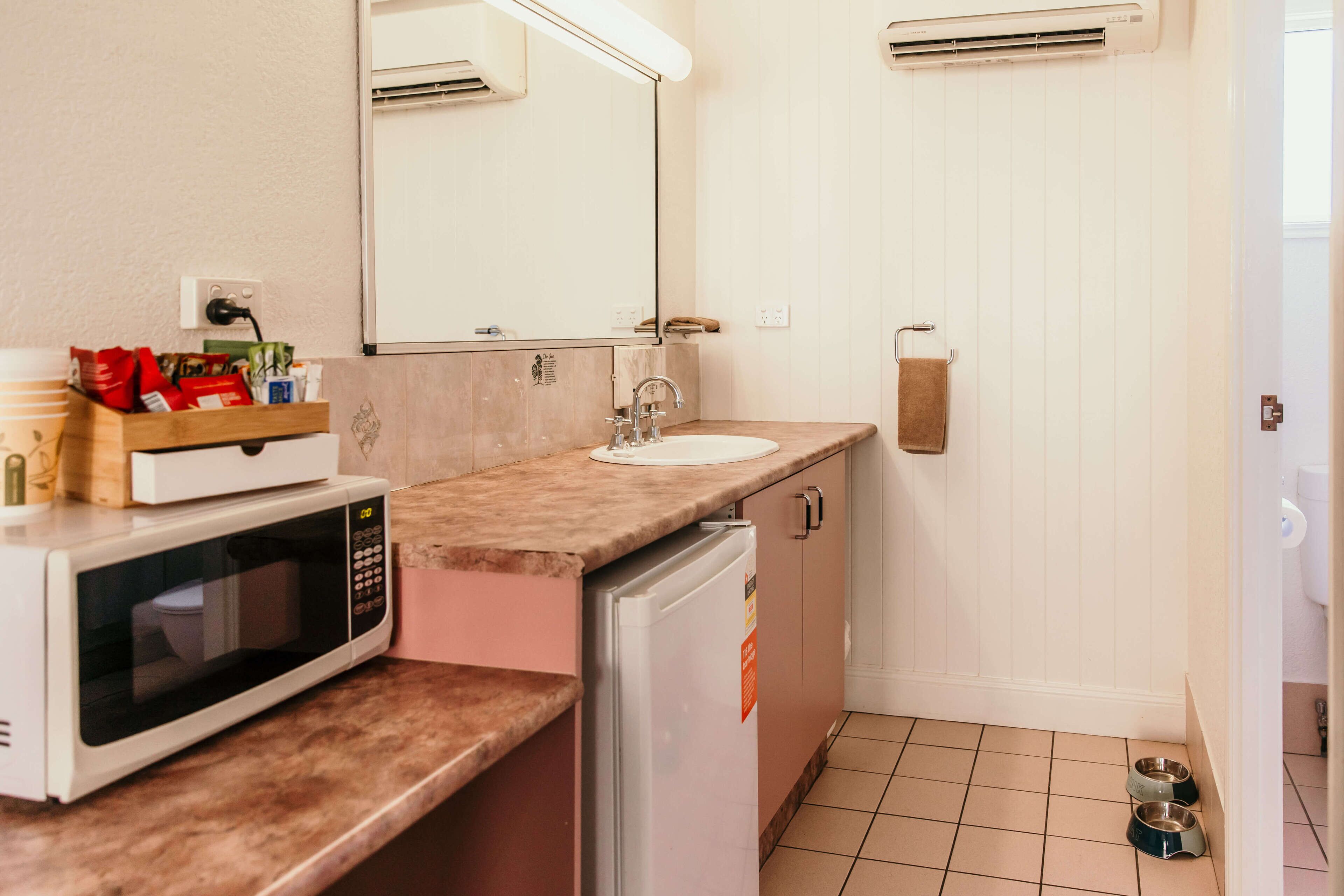 A compact bathroom with a sink, mirror, microwave, and refrigerator.