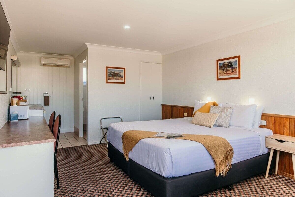 A hotel room with a bed, bedside table, and a desk area with a chair.