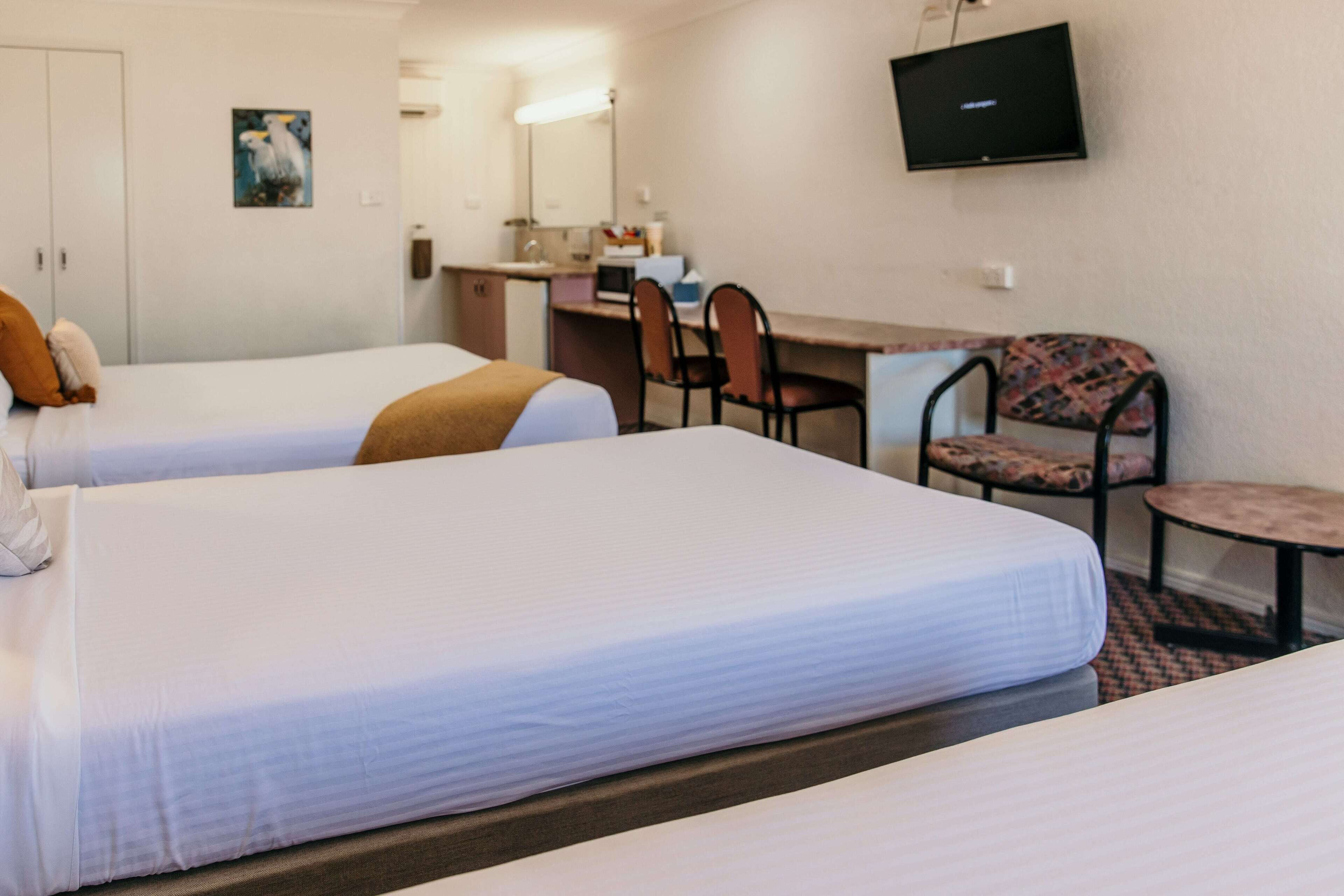 Habitación de hotel con dos camas, un escritorio, una silla y una televisión en la pared.