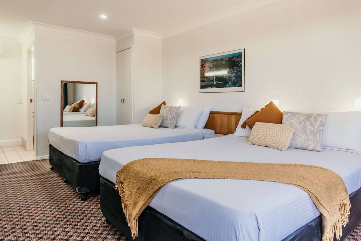 A hotel room with two beds, a large mirror, a painting on the wall, and a patterned carpet.