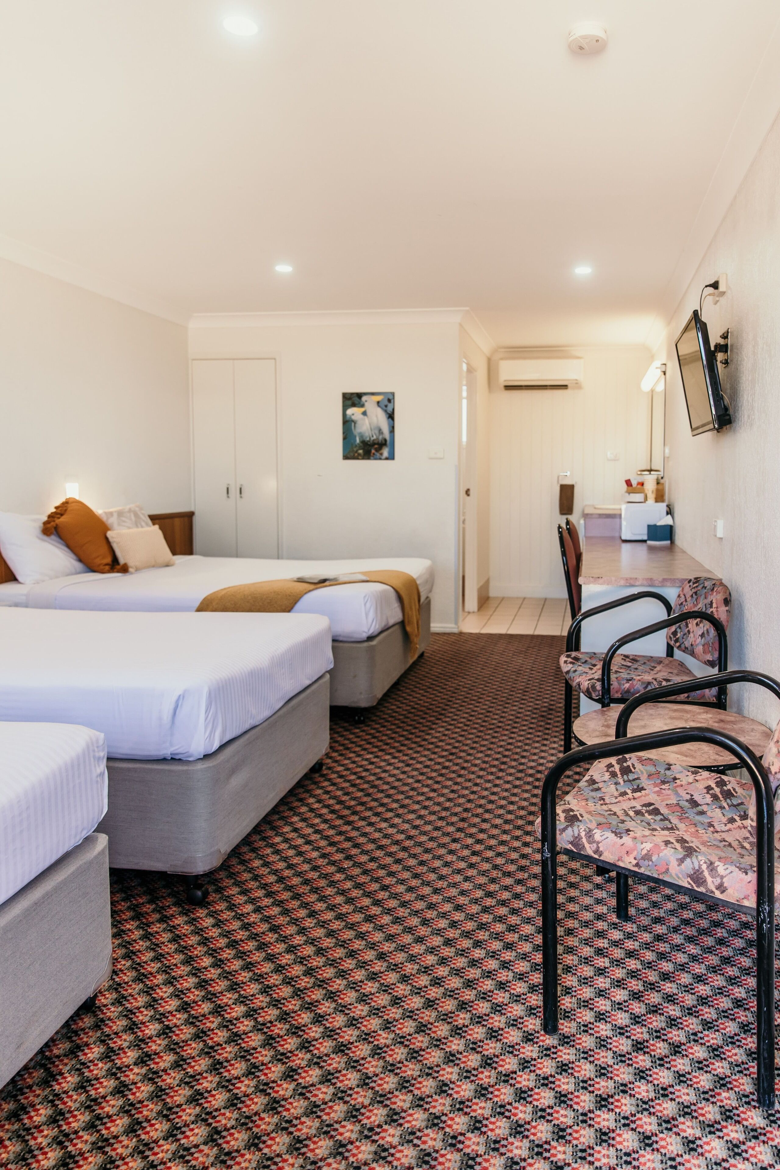 A hotel room with two beds, a desk, a chair, and a patterned carpet.