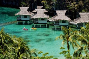 Overwater bungalows with thatched roofs, clear turquoise water, and palm trees. - Miniloc Island Resort (El Nido)