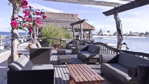 Terraza al aire libre con mobiliario de mimbre, una mesa de madera y una estructura con techo de paja.