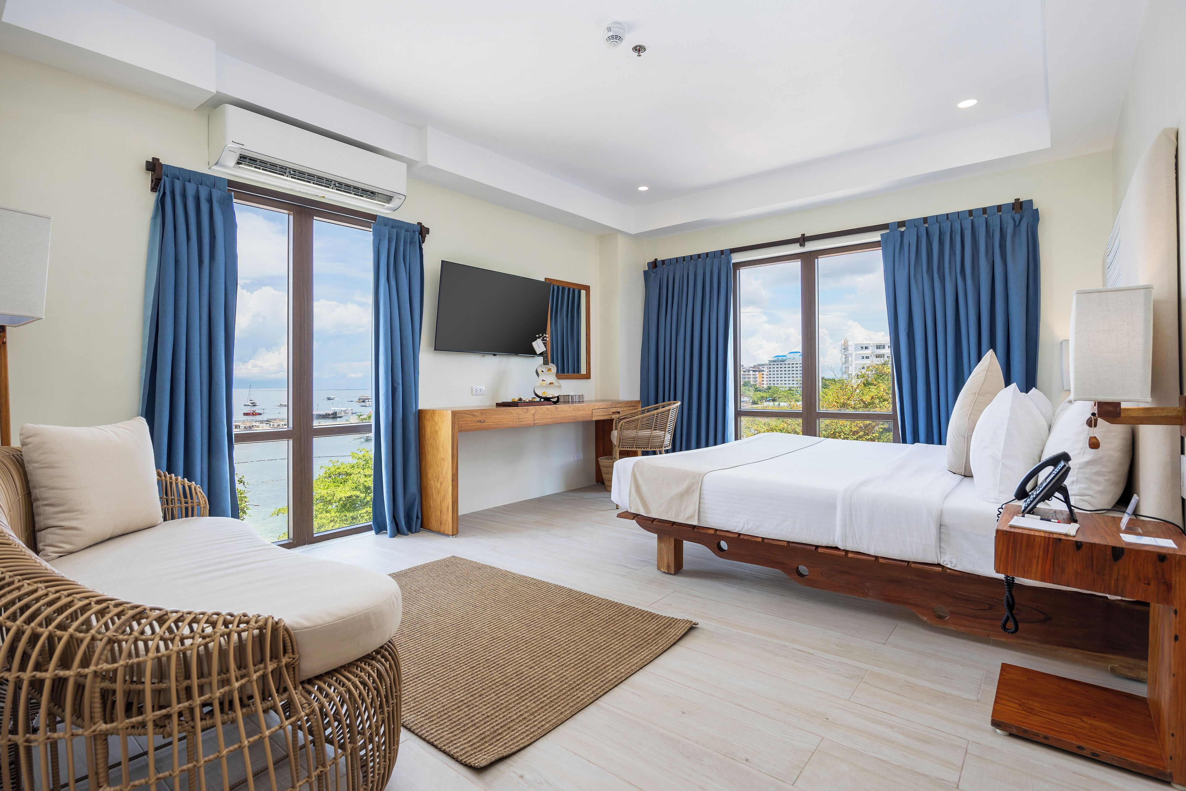 Une chambre d’hôtel avec un lit, un bureau, une chaise, une télévision et une vue sur la mer.
