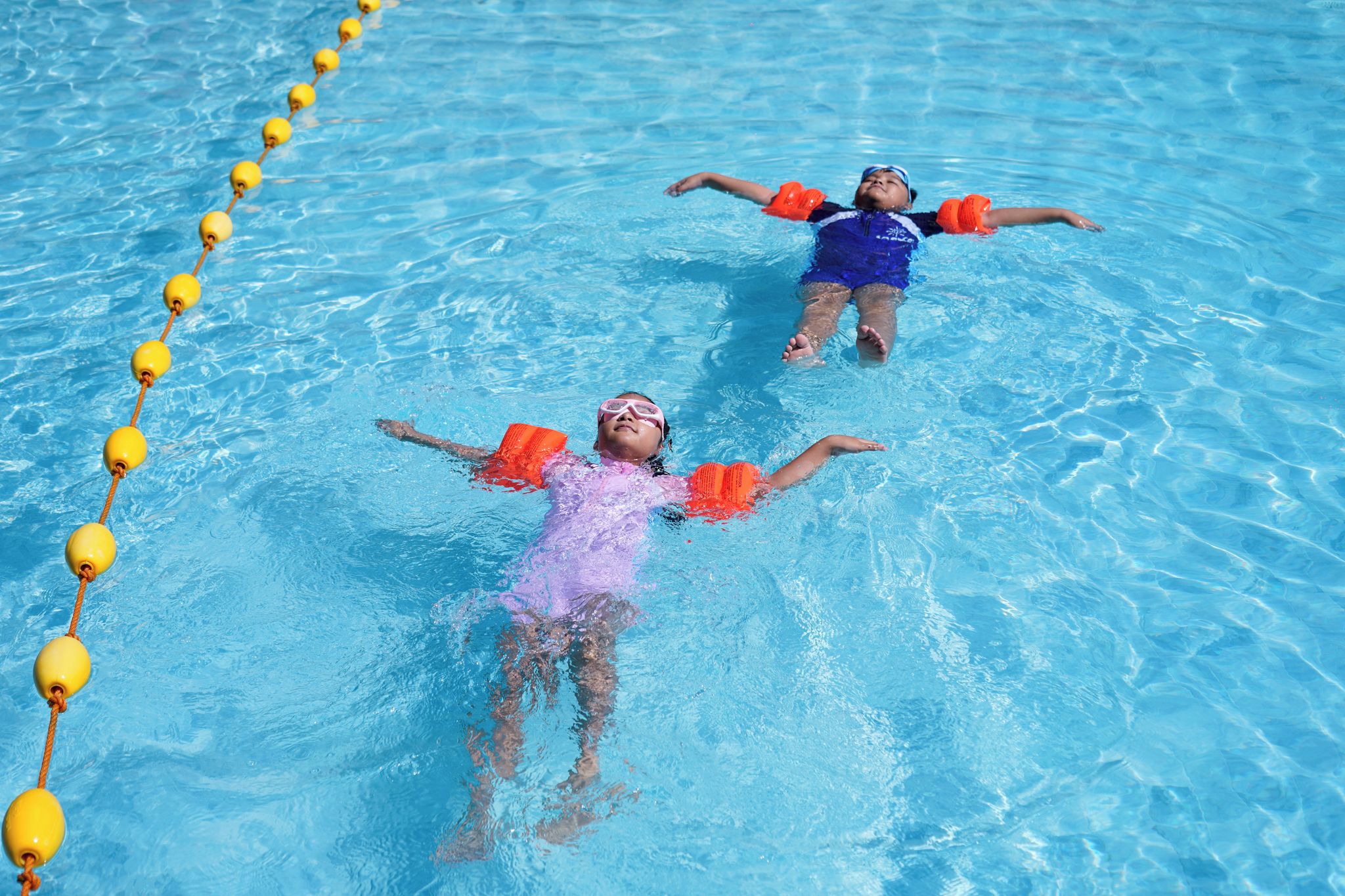 Two individuals floating in a pool with lane markers.
