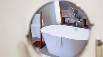 Un espejo redondo que refleja un baño con una bañera independiente, una silla de madera y un perchero.