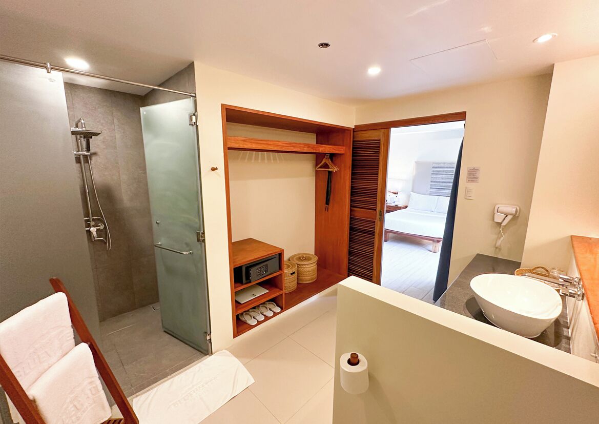 A modern bathroom with a glass shower enclosure, a wooden vanity with a sink, and a walk-in closet with shelves and baskets.