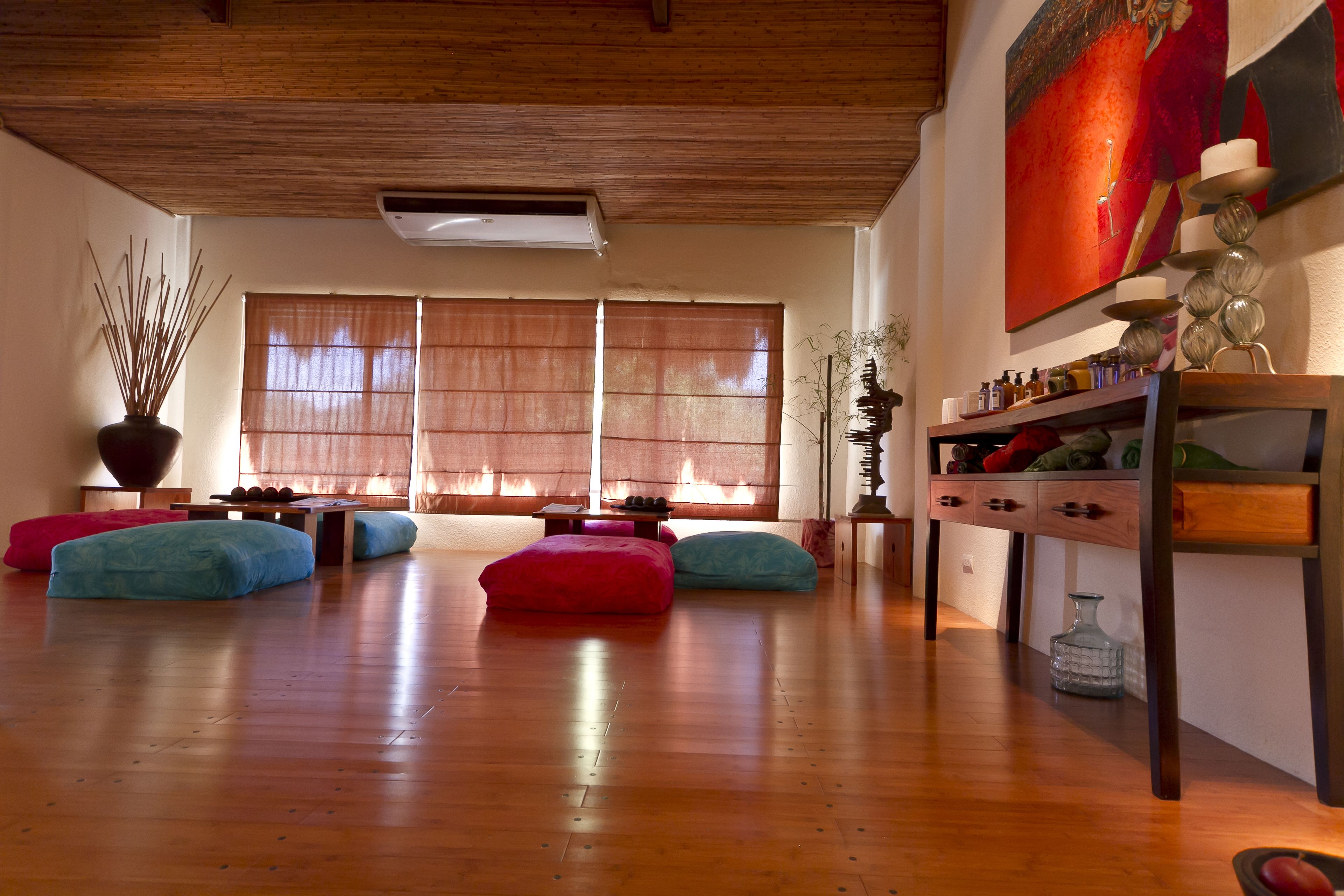 Amplia sala de estar con piso de madera, ventanas grandes con persianas de bambú y una obra de arte moderna en la pared.