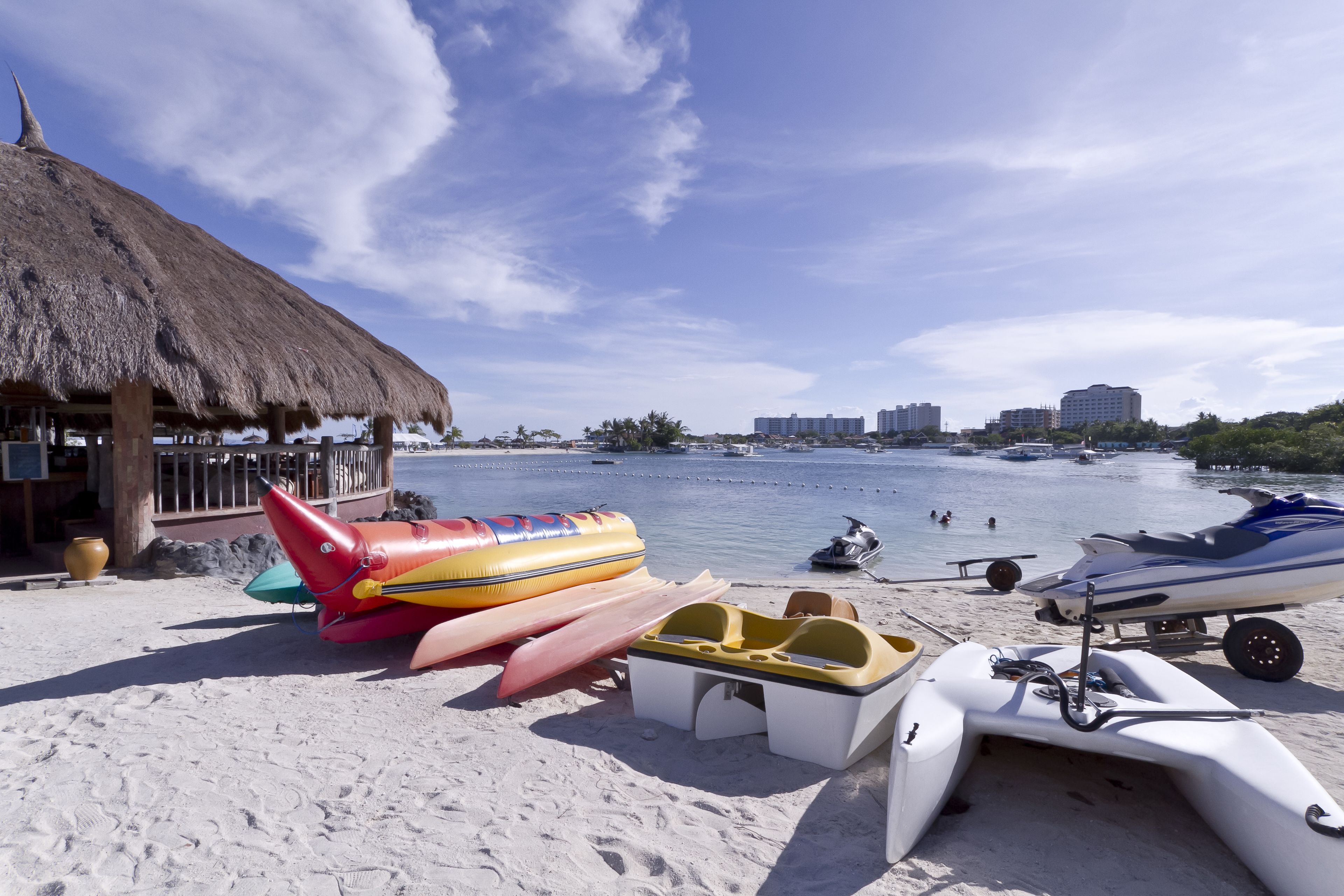Una playa con una estructura de techo de paja, lanchas inflables y un jet ski en la arena.