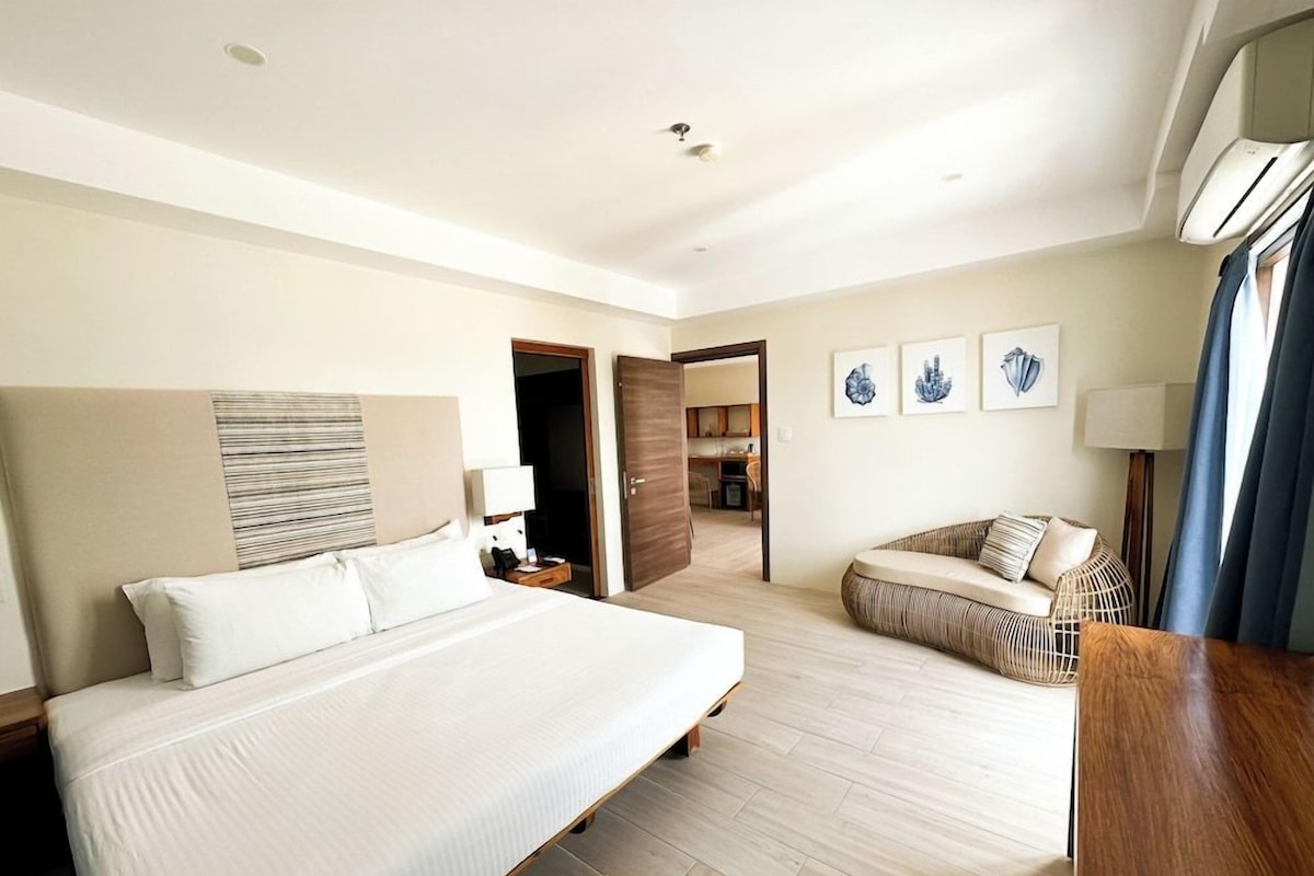 Una habitación de hotel con una cama grande, un sofá, un comedor y obras de arte en las paredes.