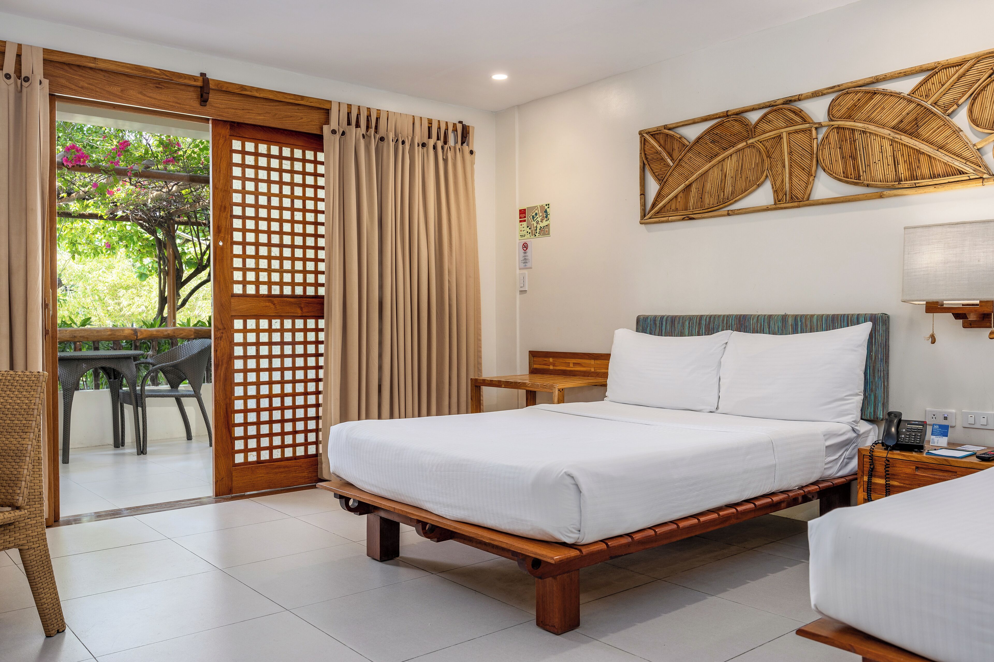 A hotel room with a wooden bed, a small desk, a chair, and a view of the outdoors through a sliding door.